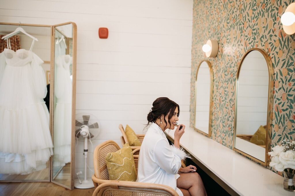 A bride in a robe sitting in front of a mirror, preparing for her wedding day.