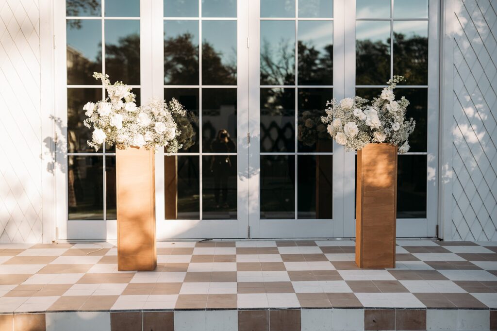 Two vases with flowers on a checkered floor at a wedding.
