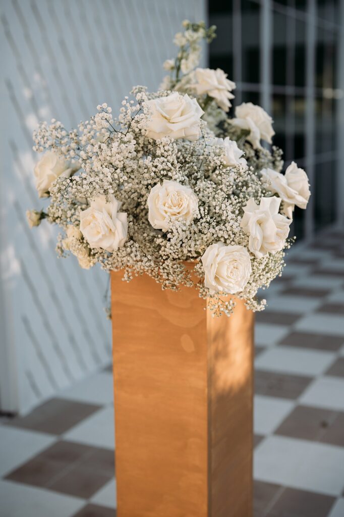 White roses in a wooden vase placed on a checkered floor, perfect for a black and white wedding.