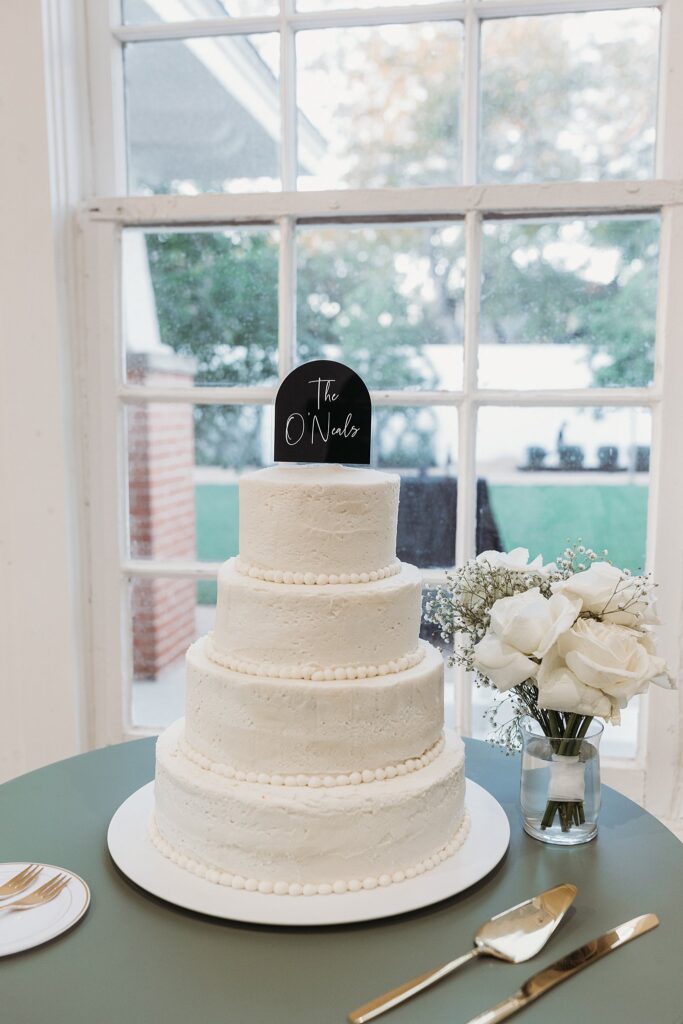 A black and white wedding cake on a table in front of a window.