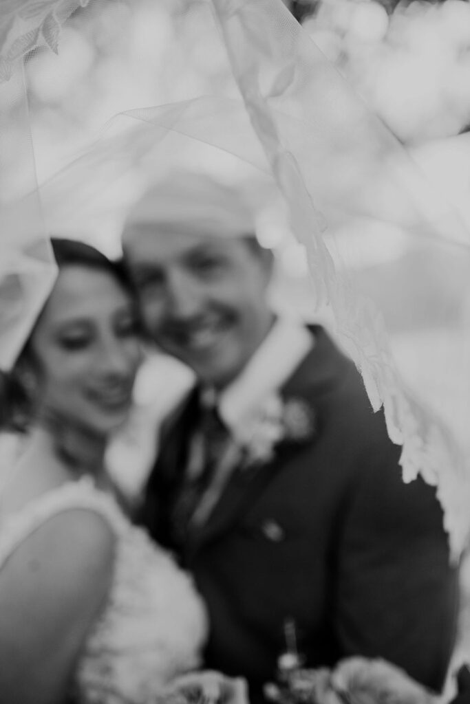A black and white photo of a bride and groom under a veil at Pecan Springs Ranch.
