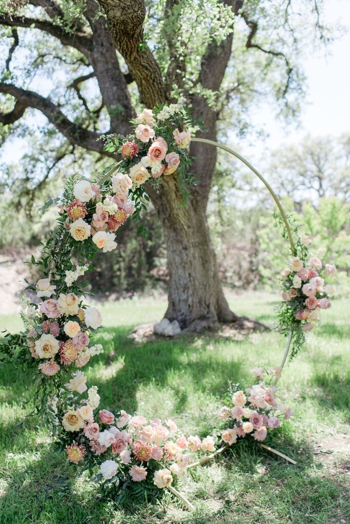 A circular arch decorated with roses in front of a tree at Pecan Springs Ranch.