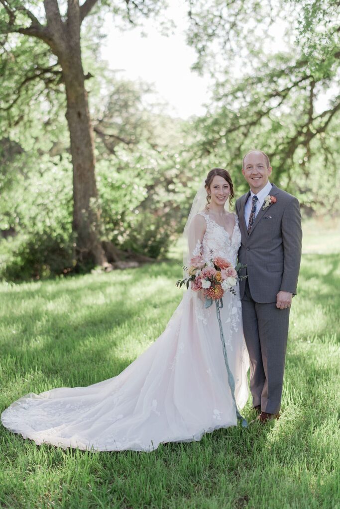 A bride and groom in a grassy field at Pecan Springs Ranch.