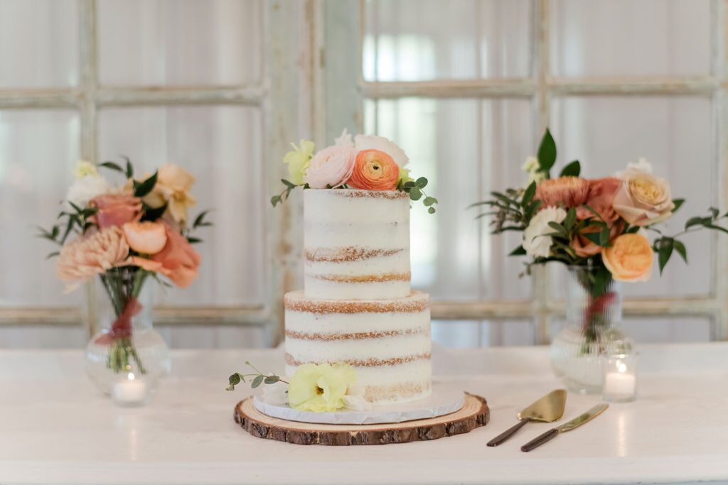 At Pecan Springs Ranch, a wedding cake is elegantly displayed on a table adorned with flowers.