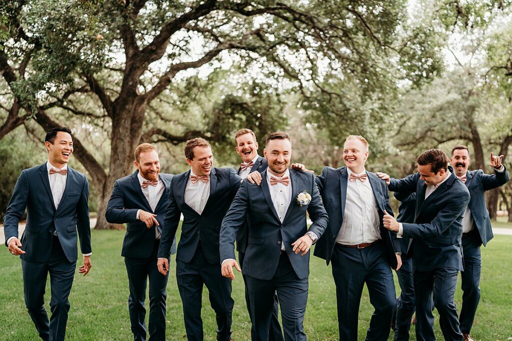 A group of groomsmen laughing in the grass.