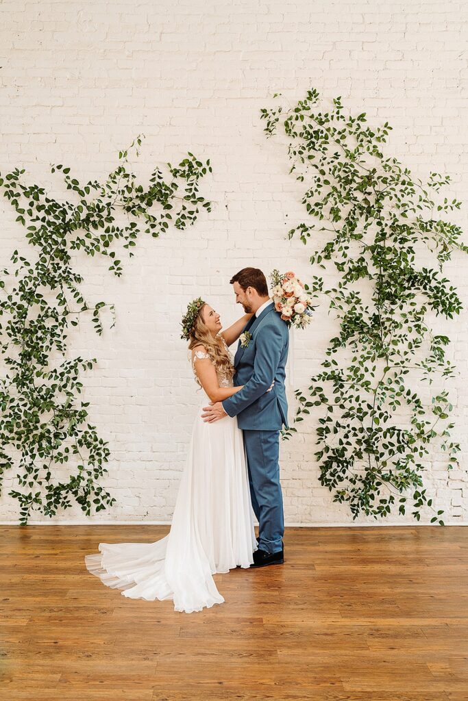 A bride and groom posing in front of an ivy covered wall.