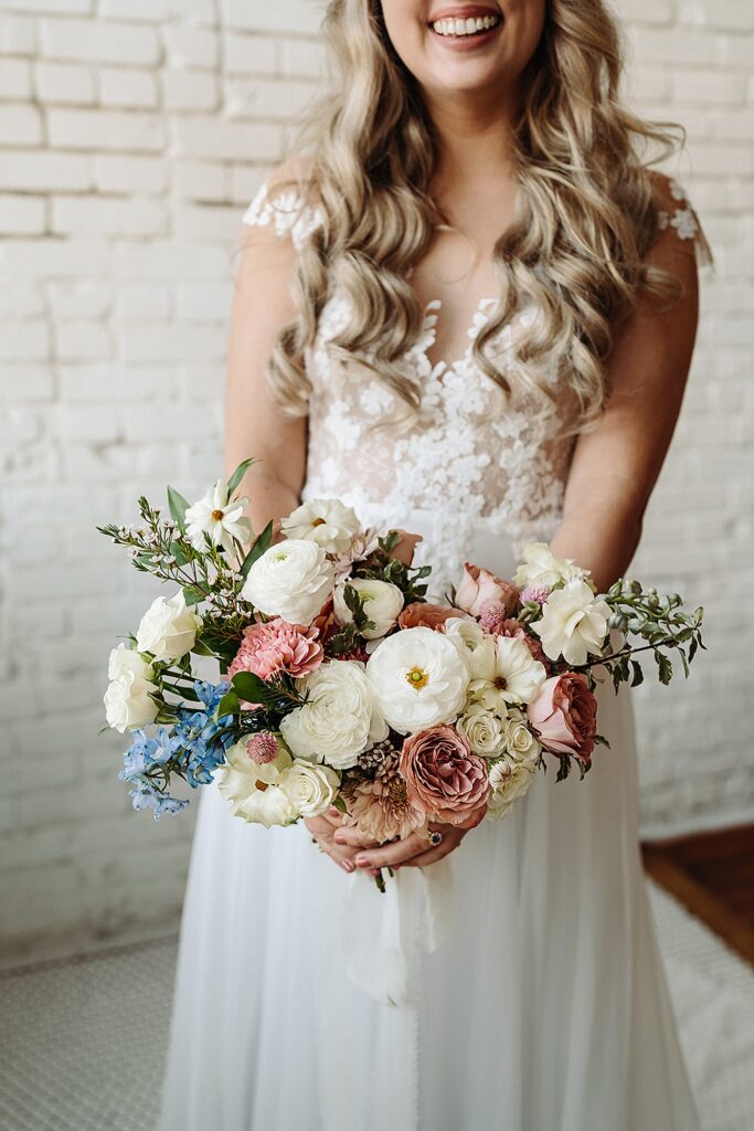A bride holding her wedding bouquet in front of a brick wall.