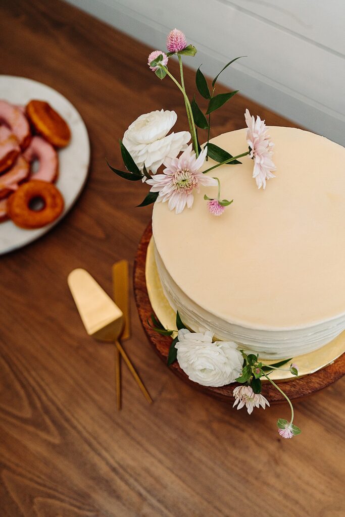A white cake with flowers and donuts on a wooden table.