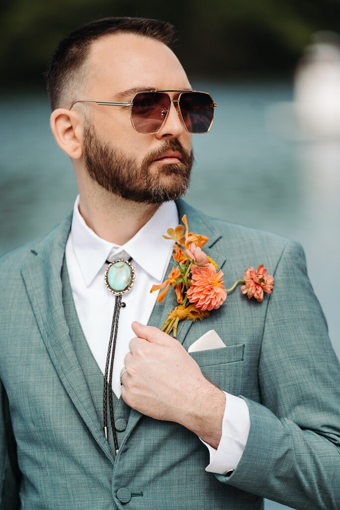 A dapper man in a suit with sunglasses and a flower on his lapel.