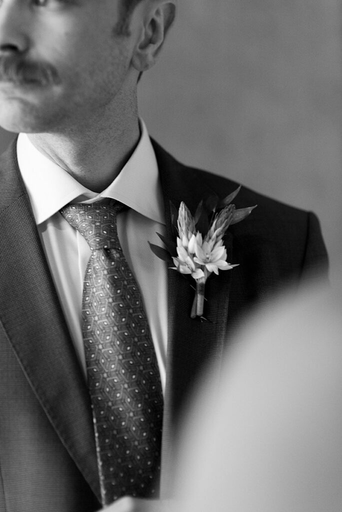 A man in a suit with a boutonniere attending a wedding ceremony.