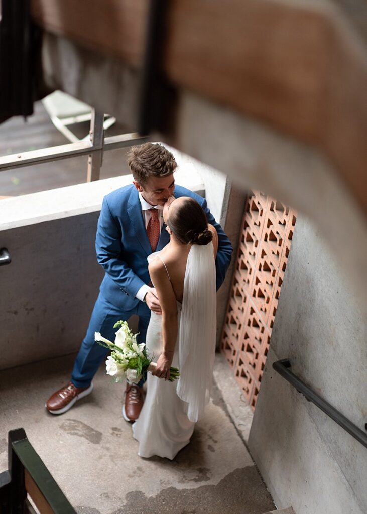 A bride and groom sharing a passionate kiss during their romantic wedding at the Carpenter Hotel, captured on a stunning staircase.