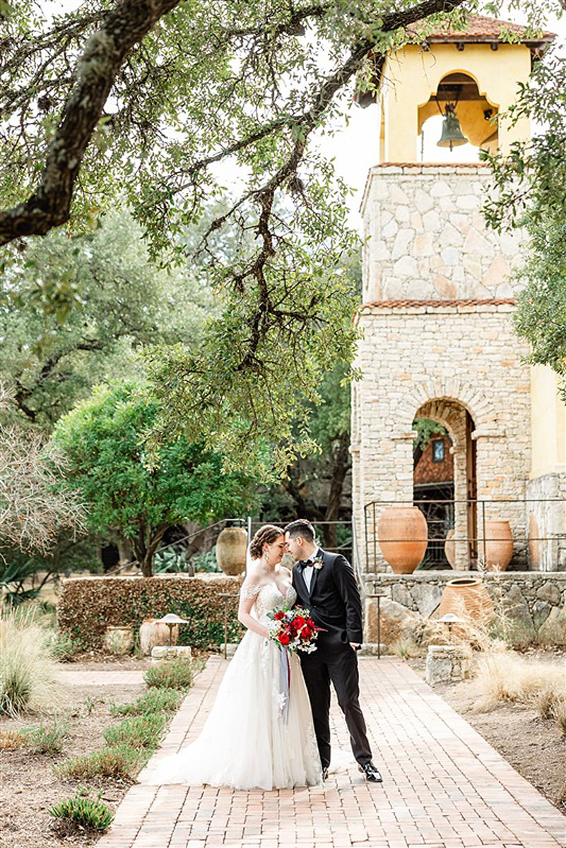 A Camp Lucy Wedding featuring a bride and groom kissing in front of a stone building.