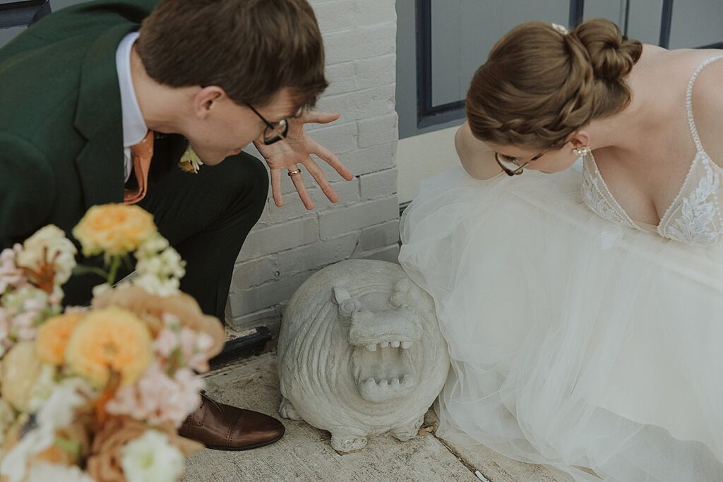 A bride and groom posing next to a statue of a hippo.