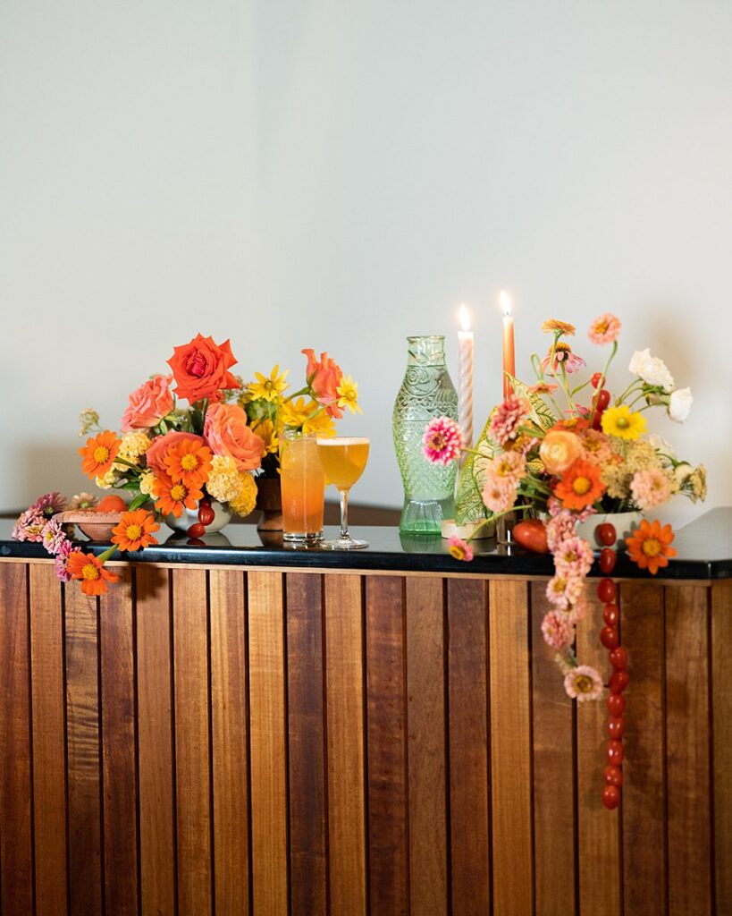 At the Hotel Magdalena, a wooden bar adorned with vibrant orange flowers and flickering candles sets the scene for an enchanting wedding celebration.