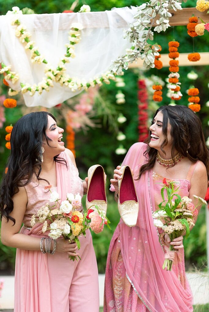 Two bridesmaids in pink saris holding bouquets.