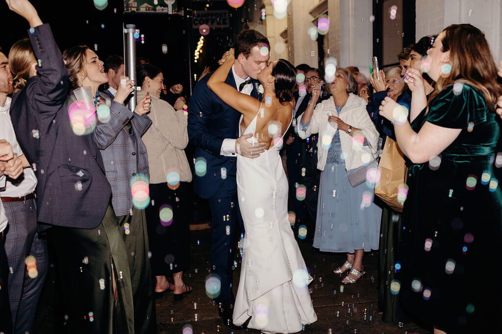 A newlywed couple sharing a kiss amidst a joyful bubble send-off at their 111 East wedding.