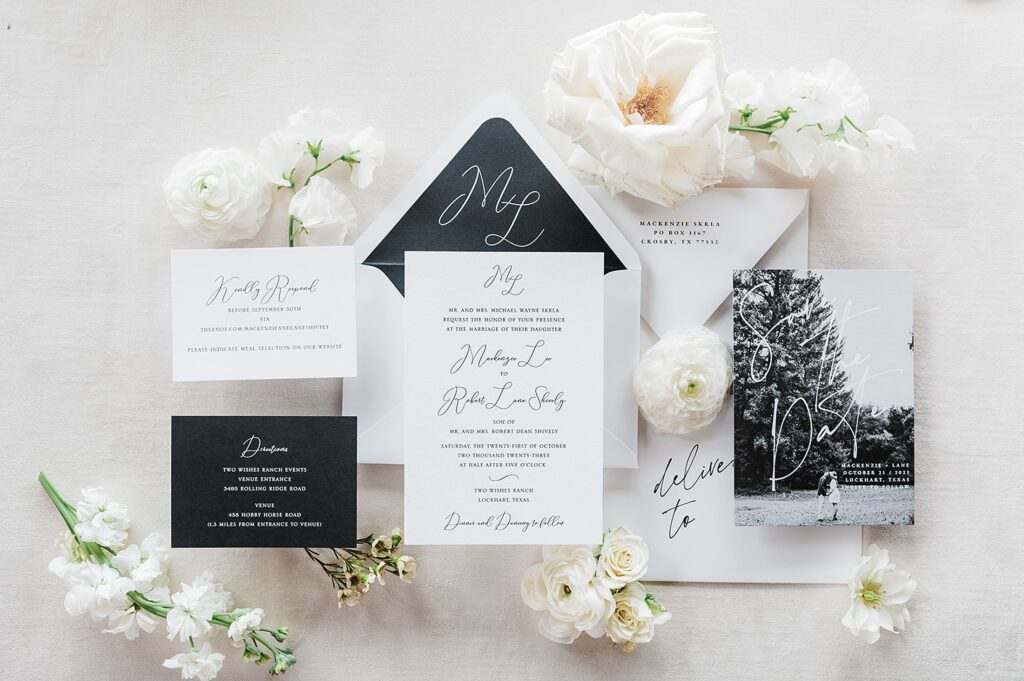 A flat lay image of elegant wedding stationery including invitation cards, RSVP cards, and envelopes, surrounded by white flowers.