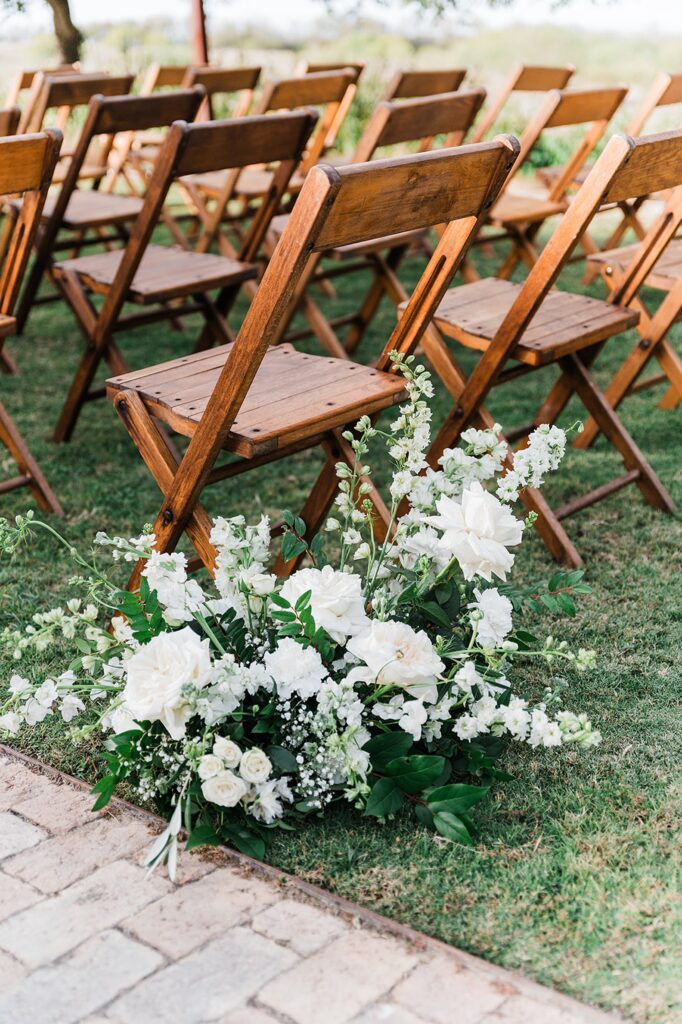 Wooden folding chairs arranged in rows on the lush grass at Two Wishes Ranch, with a large floral arrangement of white flowers and greenery adorning the front row.