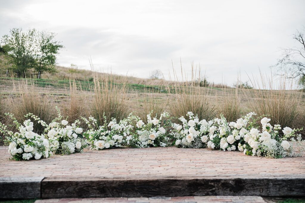 A brick walkway bordered by tall grasses and white flowers creates a serene outdoor setting at Two Wishes Ranch.