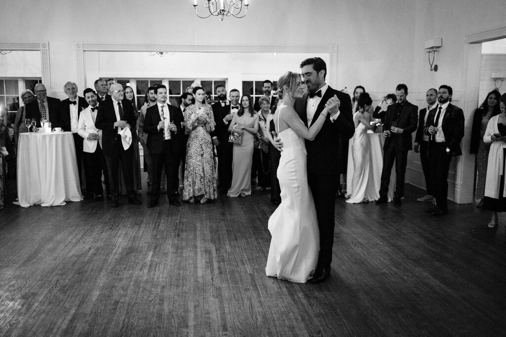 A bride and groom share a first dance in a formal room while guests in evening attire watch and stand nearby at Mattie's Austin.