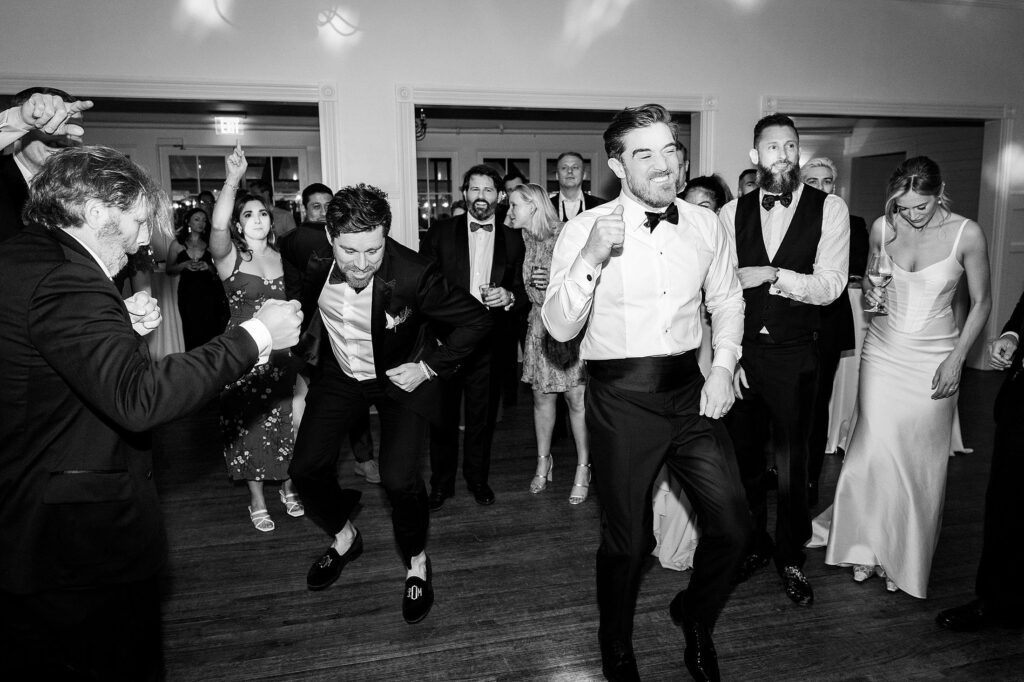 A group of well-dressed people dance energetically in a well-lit room during a formal event.