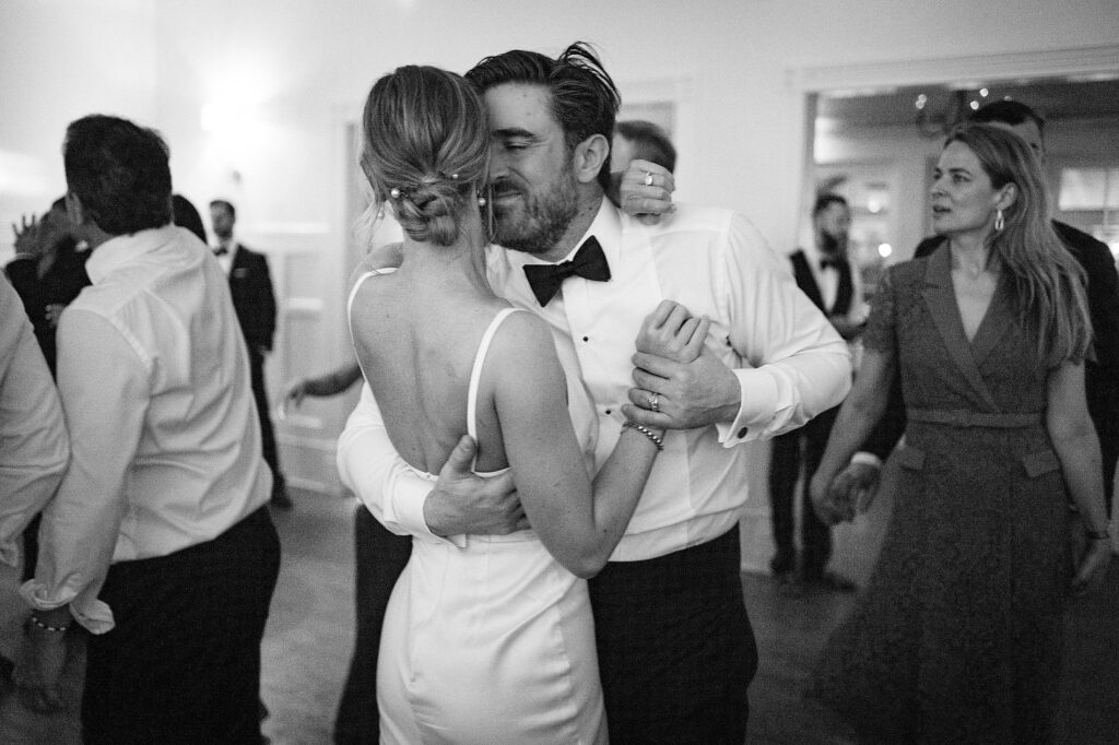 A couple dressed in formal attire shares a dance at an event, surrounded by other attendees. The man, kissed the woman’s cheek as they enjoyed a moment meticulously planned by an Austin Wedding Coordinator.