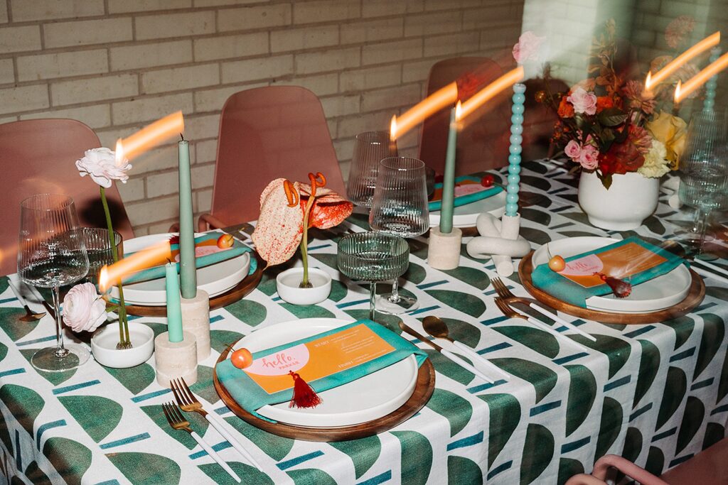 A vividly decorated dining table set for a meal, featuring a patterned tablecloth, colorful flowers, candles, glassware, and menus on plates. This stunning setting illustrates the expertise of an Austin Wedding Planner at the South Congress Hotel in creating unforgettable moments.