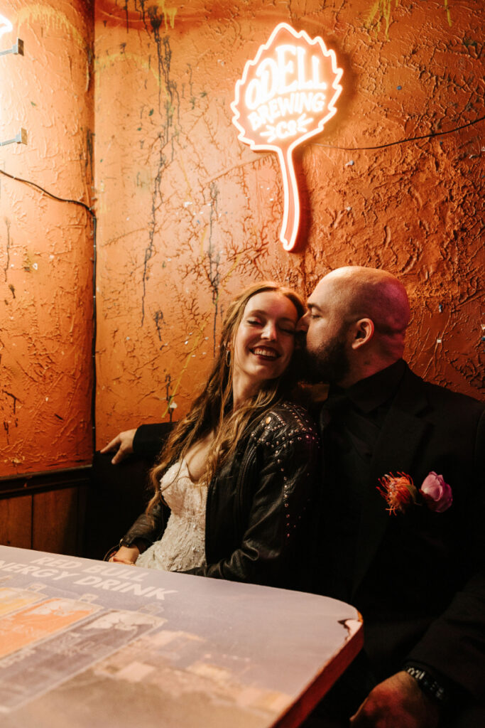 A groom kisses his smiling bride on the cheek during an after party at ODell Brewing Co.