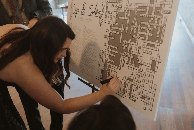 A woman fills out a giant crossword puzzle at a wedding reception, a personalized wedding idea the couple incorporated on their big day.