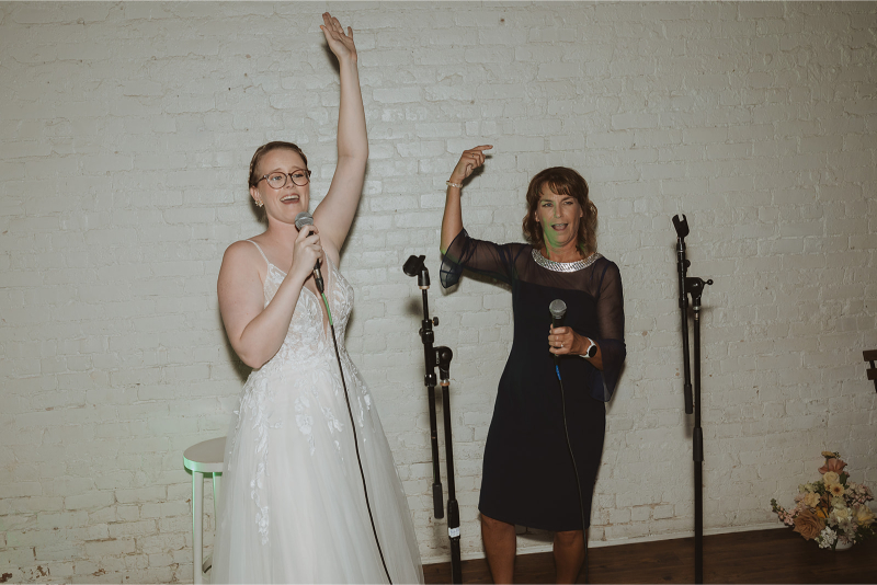 A bride and wedding guest holding microphones and singing karaoke during a wedding reception. 