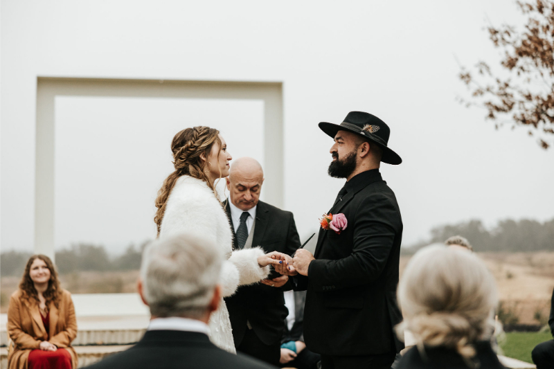 Bride and groom exchange rings during outdoor ceremony. 