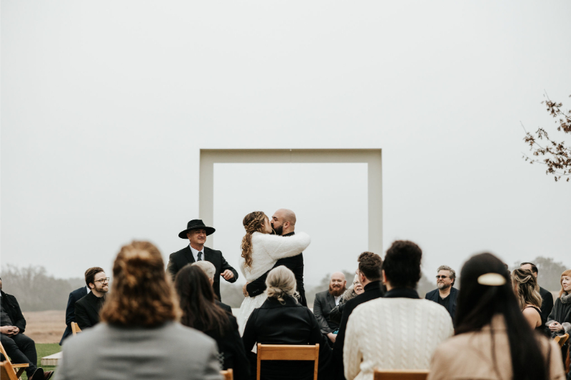 Bride and groom exchange first kiss during outdoor ceremony. 