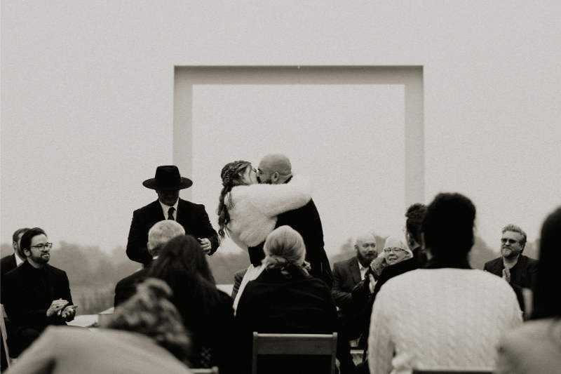 Bride and groom exchange first kiss during outdoor ceremony. 