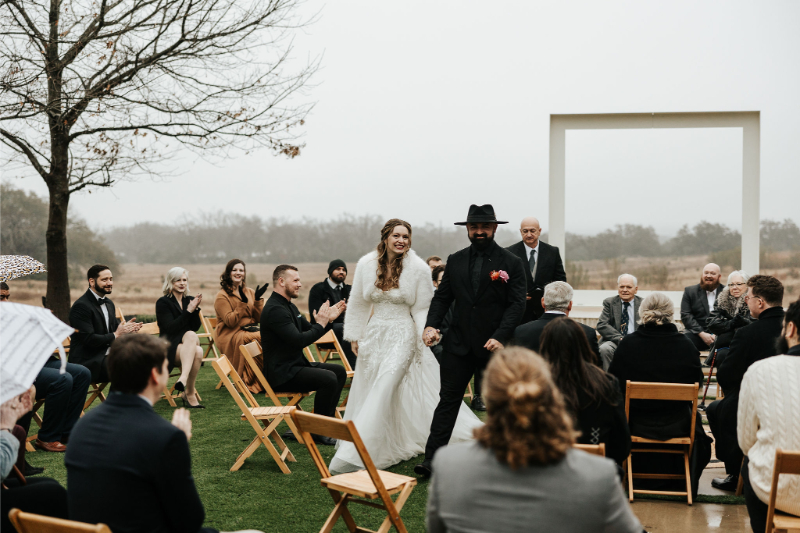 Bride and groom exit ceremony, cheering with and high-fiving guests as they walk by.