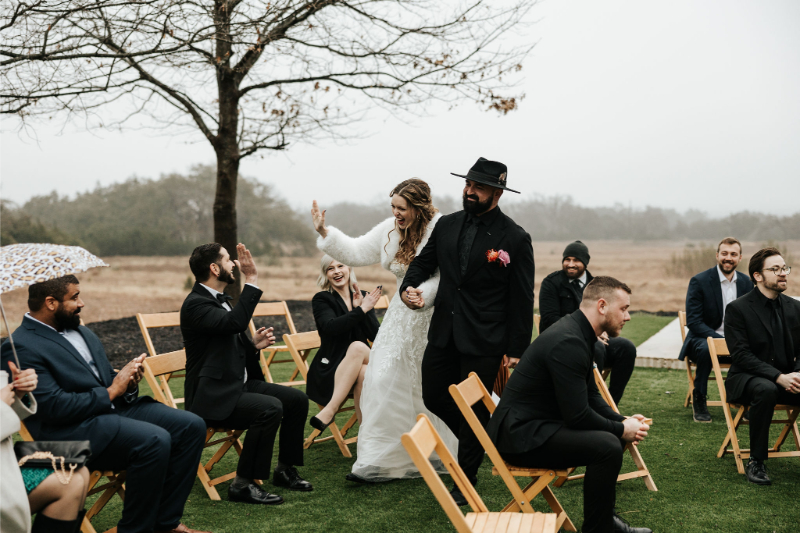 Bride and groom exit ceremony, cheering with and high-fiving guests as they walk by.