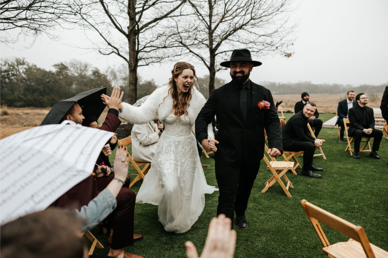 Bride and groom exit ceremony, cheering with and high-fiving guests as they walk by.