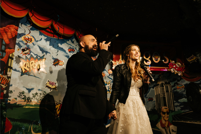 Bride and groom sing karaoke together during wedding afterparty. 