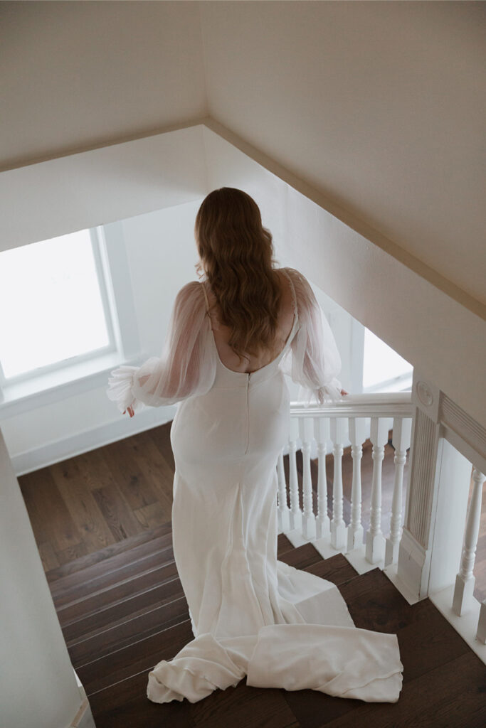 Bride descends a wooden staircase in The Grand Lady Austin, with sunlight streaming through a window.