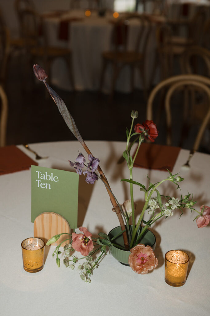 Table centerpiece featuring floral arrangement, candles, and table number for a wedding.