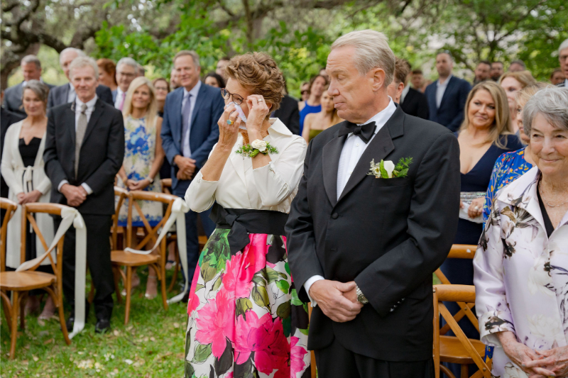 An older man and woman stand at a wedding ceremony. The woman wipes a tear as the couple shares their vows, it's what wedding guests will remember most from the day.