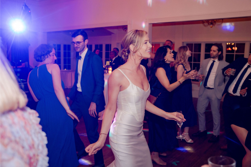 People in formal attire are dancing and socializing at an indoor event, with colorful lighting and a lively atmosphere.