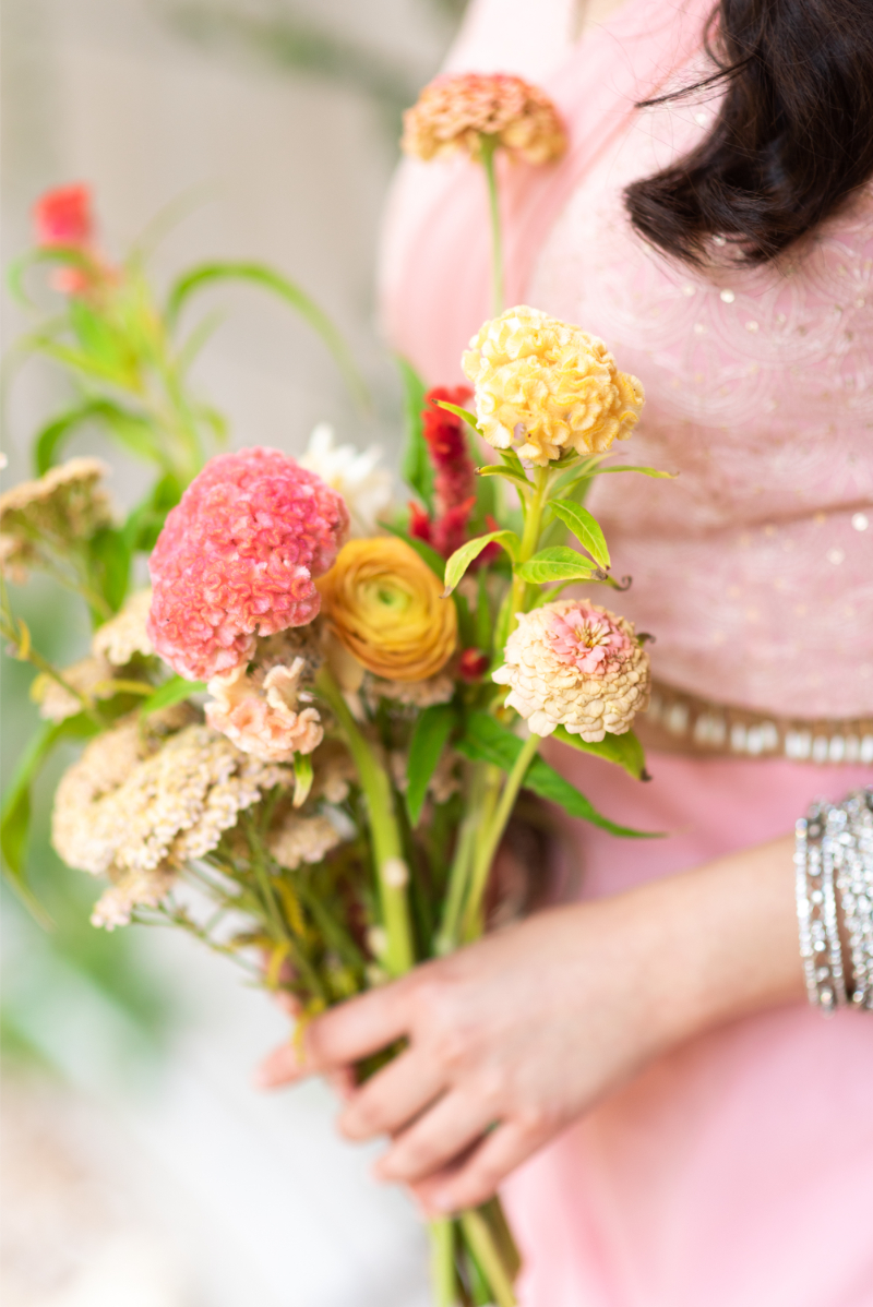 A person in a pink dress holding a vibrant bouquet of flowers, including yellow and pink blooms, with their face not visible.