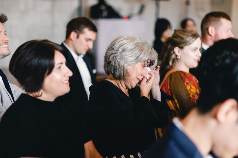 A woman wipes tears from her eyes while seated among other well-dressed guests at an indoor event at One Eleven East Hutto.