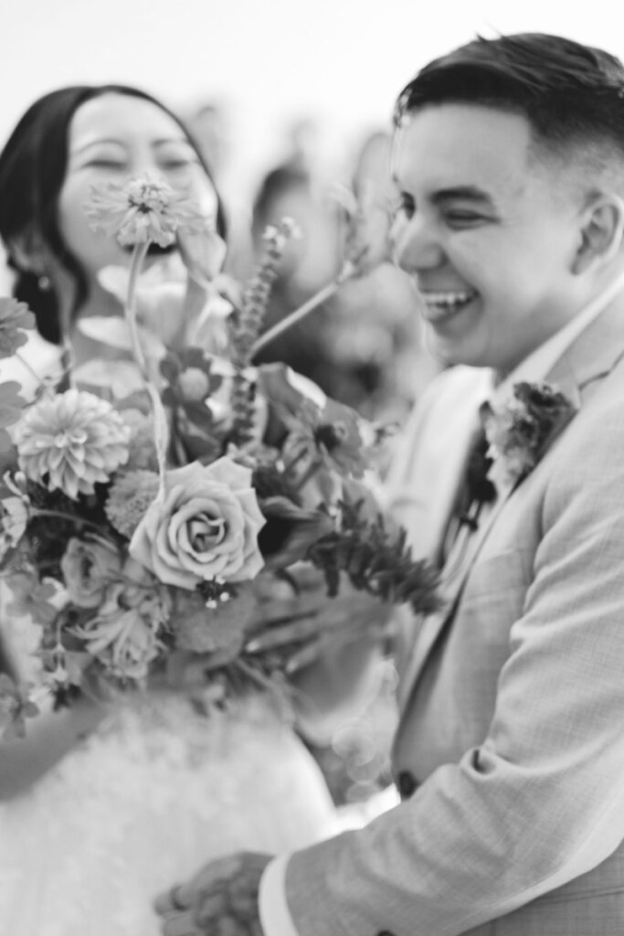 Black and white photo of a smiling couple holding a bouquet of flowers at One Eleven East Hutto, with the focus on their joyful expressions.