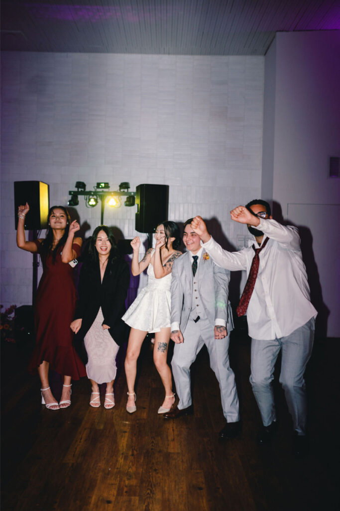 Five people dressed in formal attire are dancing together at an indoor event at One Eleven East Hutto, with speakers and lights illuminating the background.