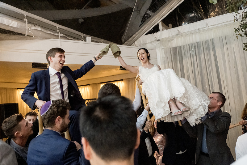 A bride and groom are lifted on chairs by guests at their wedding venue in Austin.