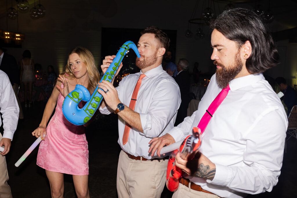 A group of people playing a blow up saxophone as they hit the dance floor during a wedding weekend.