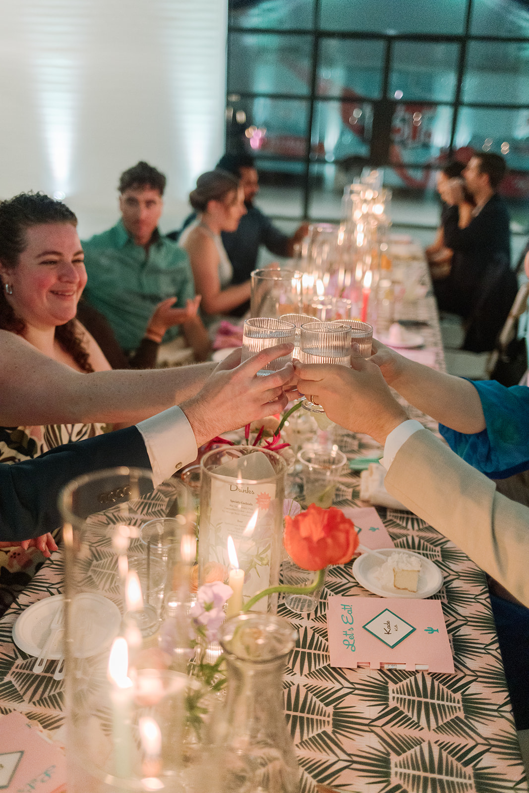 A group of people sitting at a decorated dinner table clink glasses in a toast, with candles and flowers arranged along the center. A perfect example of a guest-centered wedding weekend.