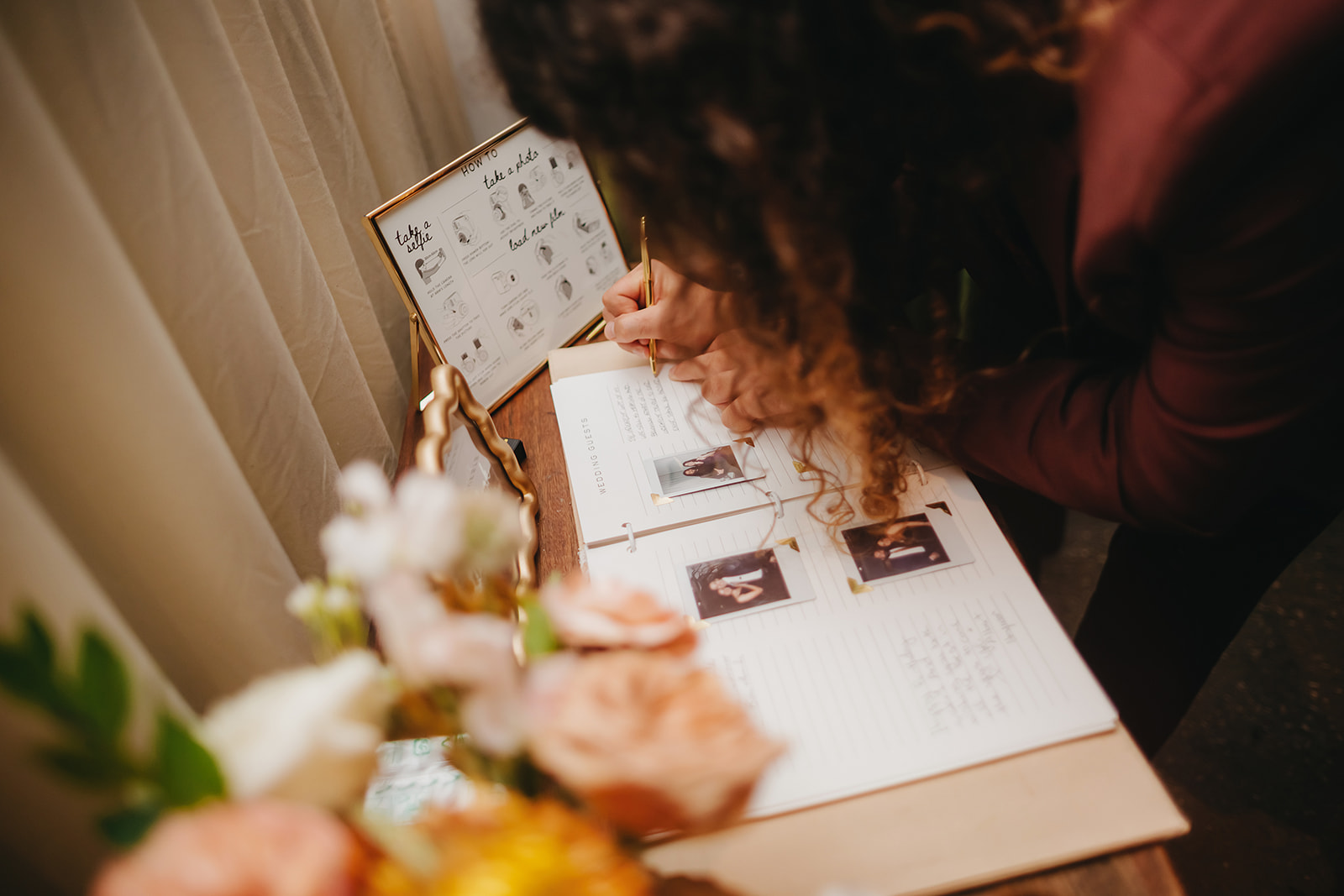 A person writes in a guest book on a table with flowers and a display showing a guide for leaving messages.