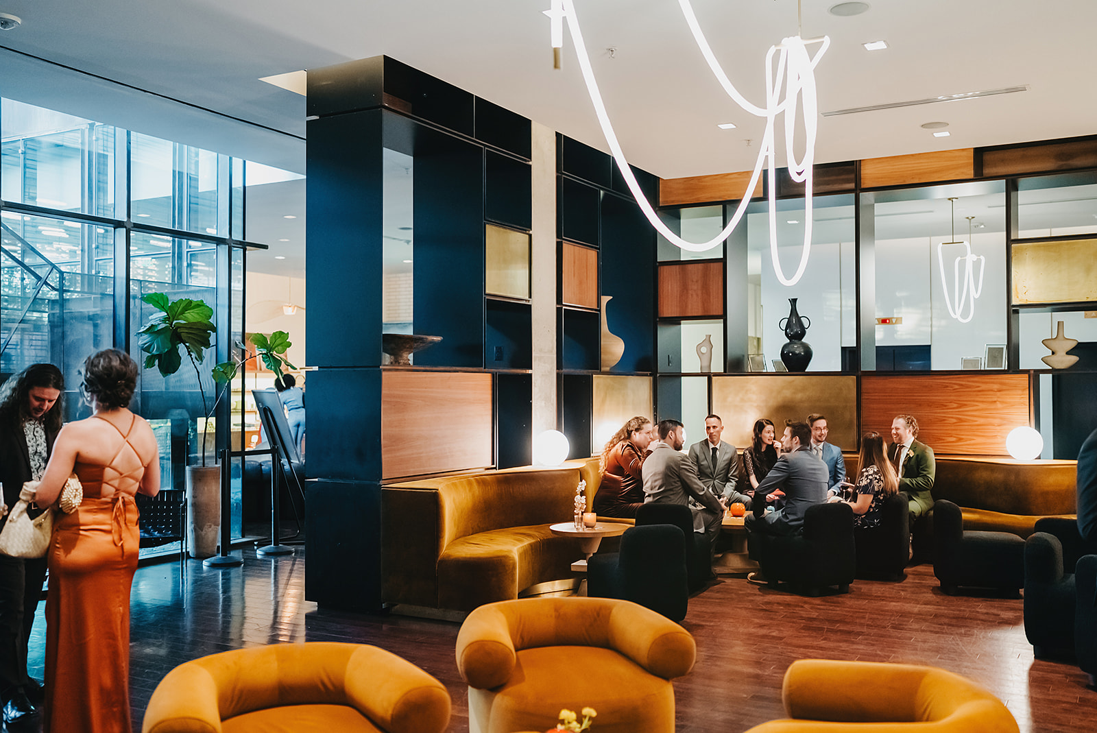 People are seated on brown sofas in a modern lounge at South Congress Hotel in Austin with contemporary decor and large windows; a few others are standing and talking.